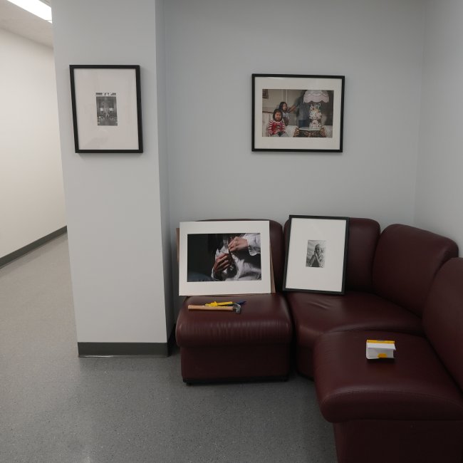 Some framed works hanging on wall with others resting on a red couch near tools, waiting to be installed