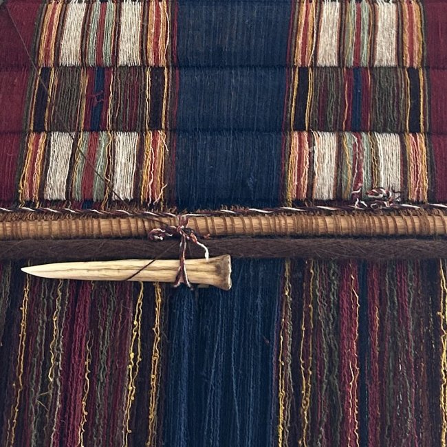 Close up image of natural dye fibers woven on a loom with a weaving tool